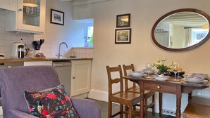 A dining area with a table set for two, a purple armchair, and a kitchen in the background. - Charming Snowdonia Cottage for 4 (Betws-Y-Coed)