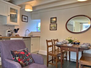 A dining area with a table set for two, a purple armchair, and a kitchen in the background. - Charming Snowdonia Cottage for 4 (Betws-Y-Coed)