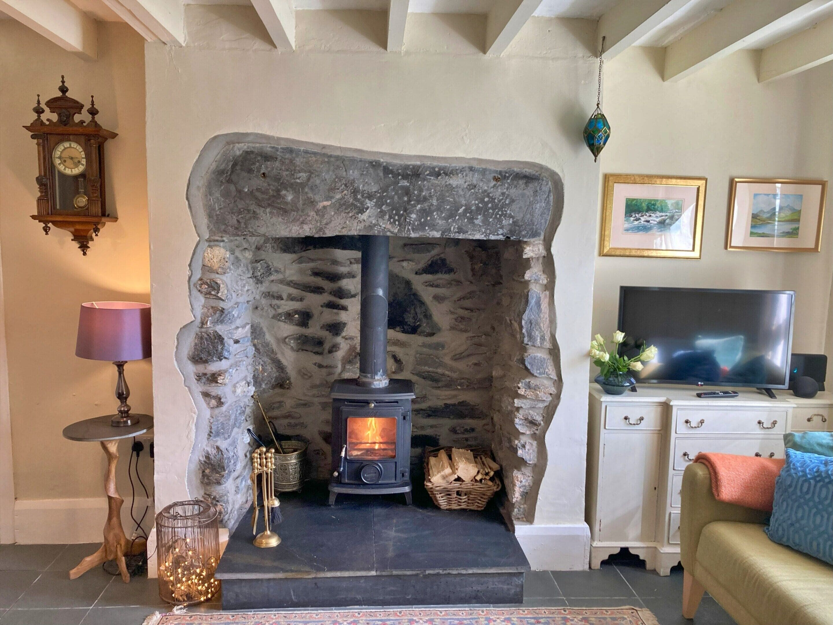 Una chimenea de piedra con estufa de leña, un reloj, un televisor y un sofá en una sala de estar.