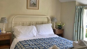 A bedroom with a bed, two bedside tables, a lamp, a framed picture on the wall, and a window with curtains. - Charming Snowdonia Cottage for 4 (Betws-Y-Coed)