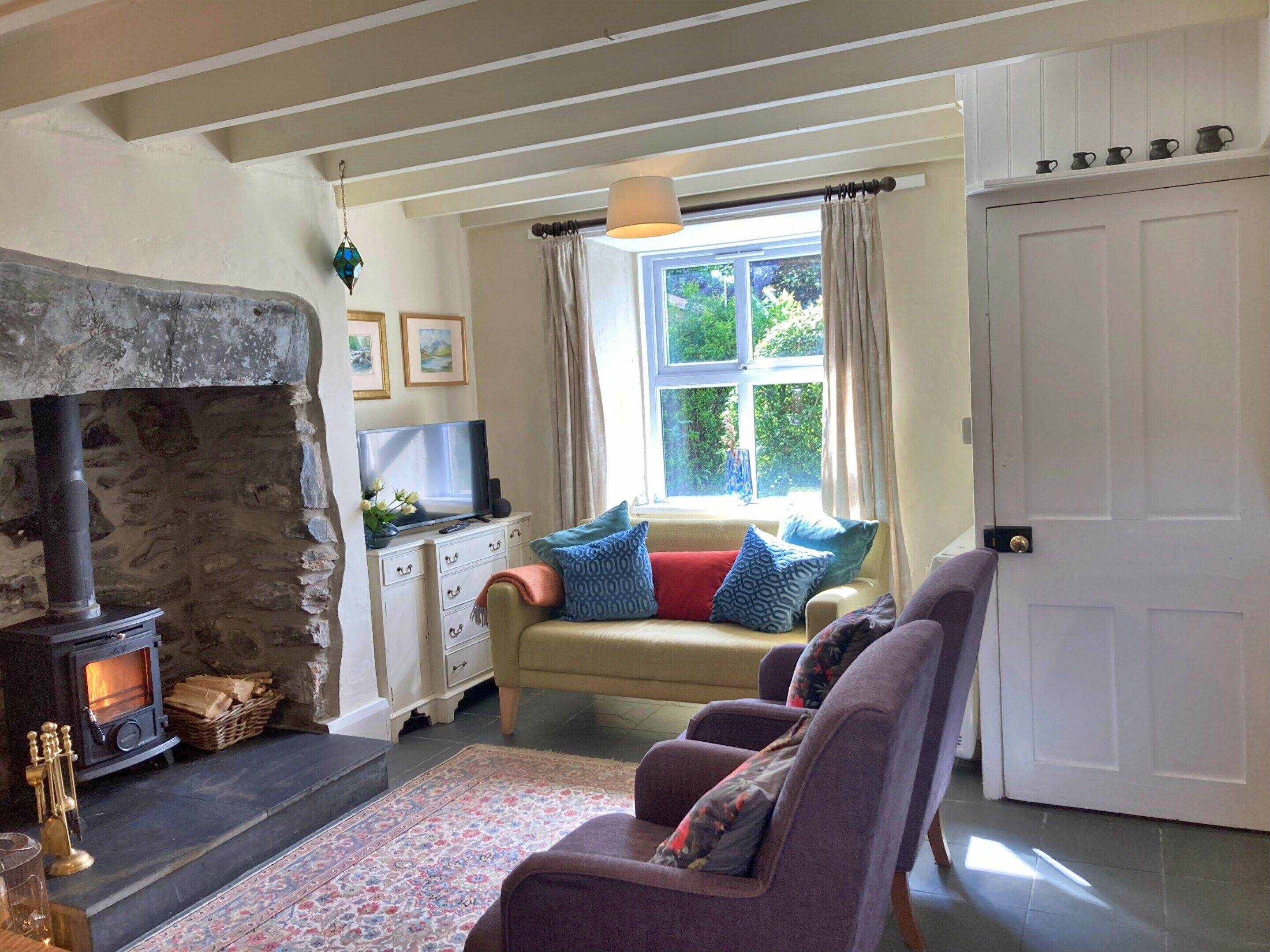 A cozy living room with a stone fireplace, a sofa set, a television, and a window with curtains.