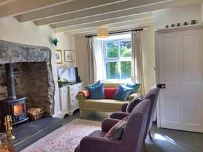 A cozy living room with a stone fireplace, a sofa set, a television, and a window with curtains. - Charming Snowdonia Cottage for 4 (Betws-Y-Coed)