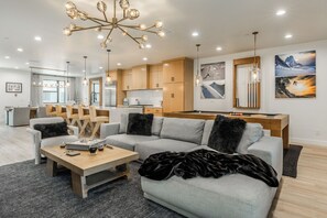 Een moderne woonkamer met een grijze hoekbank, een houten salontafel en een open haard.