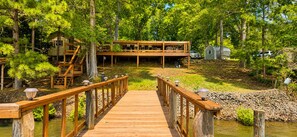 A wooden deck leading to a cabin with a second level, surrounded by trees and a body of water. - The Reel Retreat Fish, Relax & Unwind on Toledo Bend (Hemphill)