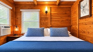 Et rum med træpaneler, en seng, to puder, en vægmonteret lampe og et vindue med persienner.