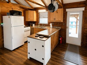 Een keuken met houten kasten, een witte koelkast, een fornuis en een raam met jaloezieën.