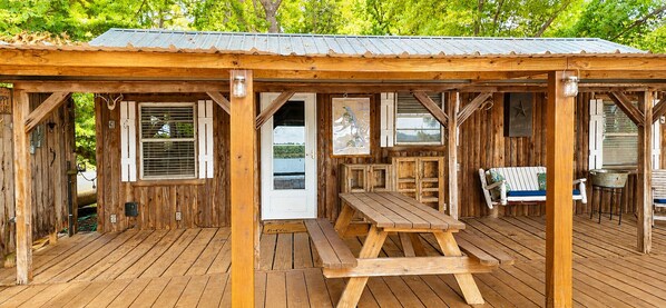 Een houten vakantiehuisje met een overdekt terras, een eettafel en een bankje.