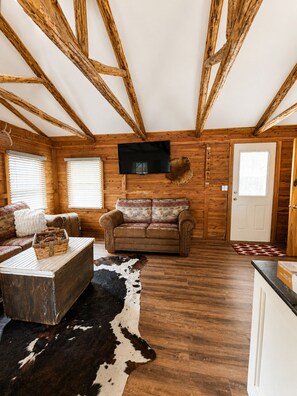A rustic cabin interior with wooden beams, a television, a sofa, a coffee table, and a cowhide rug. - The Reel Retreat Fish, Relax & Unwind on Toledo Bend (Hemphill)