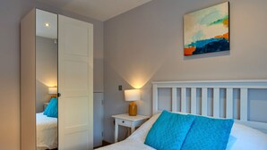 A hotel room with a bed, a nightstand, a lamp, a painting on the wall, and a wardrobe. - Scenic Lake View House for 8 (Torpoint)