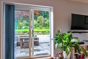 A room with a sliding glass door leading to a garden, a television mounted on the wall, and a potted plant on a table. - Scenic Lake View House for 8 (Torpoint)