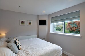 A bedroom with a bed, a television mounted on the wall, and a window with a view of trees. - Scenic Lake View House for 8 (Torpoint)