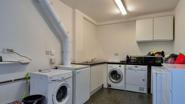 A laundry room with two washing machines, a dryer, a mop, and a broom. - Scenic Lake View House for 8 (Torpoint)