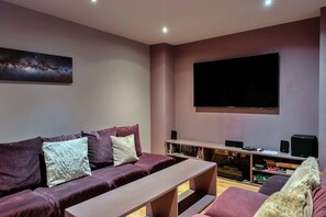 Una sala moderna con un televisor de pantalla plana grande, un sofá, una mesa de centro y una estantería con diversos objetos.