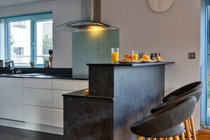 Una cocina moderna con una isla central, taburetes de bar y alimentos para el desayuno.