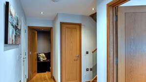 A hallway with wooden flooring, a closed door, and a staircase leading to another level. - Scenic Lake View House for 8 (Torpoint)