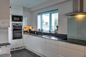 Una cocina moderna con armarios blancos, horno empotrado, microondas y campana extractora de acero inoxidable.