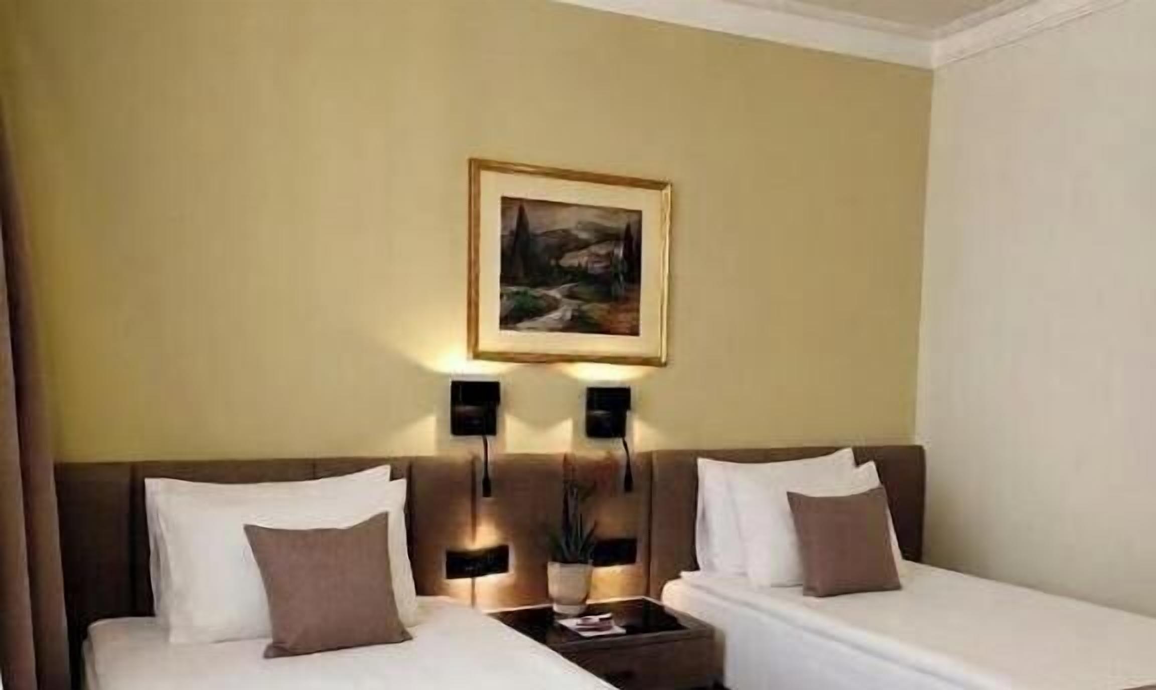 Habitación de hotel con dos camas, una mesita de noche, un cuadro en la pared y dos lámparas de pared.