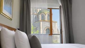 A hotel room with a bed, a view of a building through the window, and a painting on the wall.