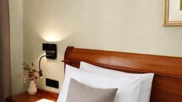 Habitación de hotel con cabecera de madera, cama con ropa de cama blanca, lámpara de noche y un jarrón con flores en la mesita de noche.