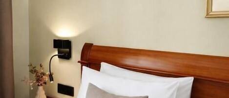 Ein Hotelzimmer mit hölzernem Kopfteil, einem Bett mit weißer Bettwäsche, einer Nachttischlampe und einer Vase mit Blumen auf dem Nachttisch.