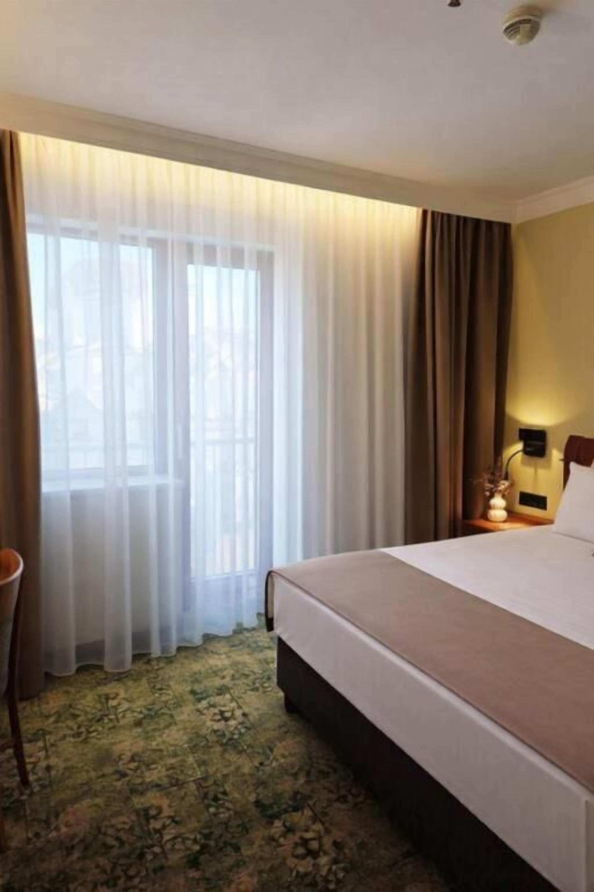 Una habitación de hotel con cama, cortinas, mesita de noche y lámpara.