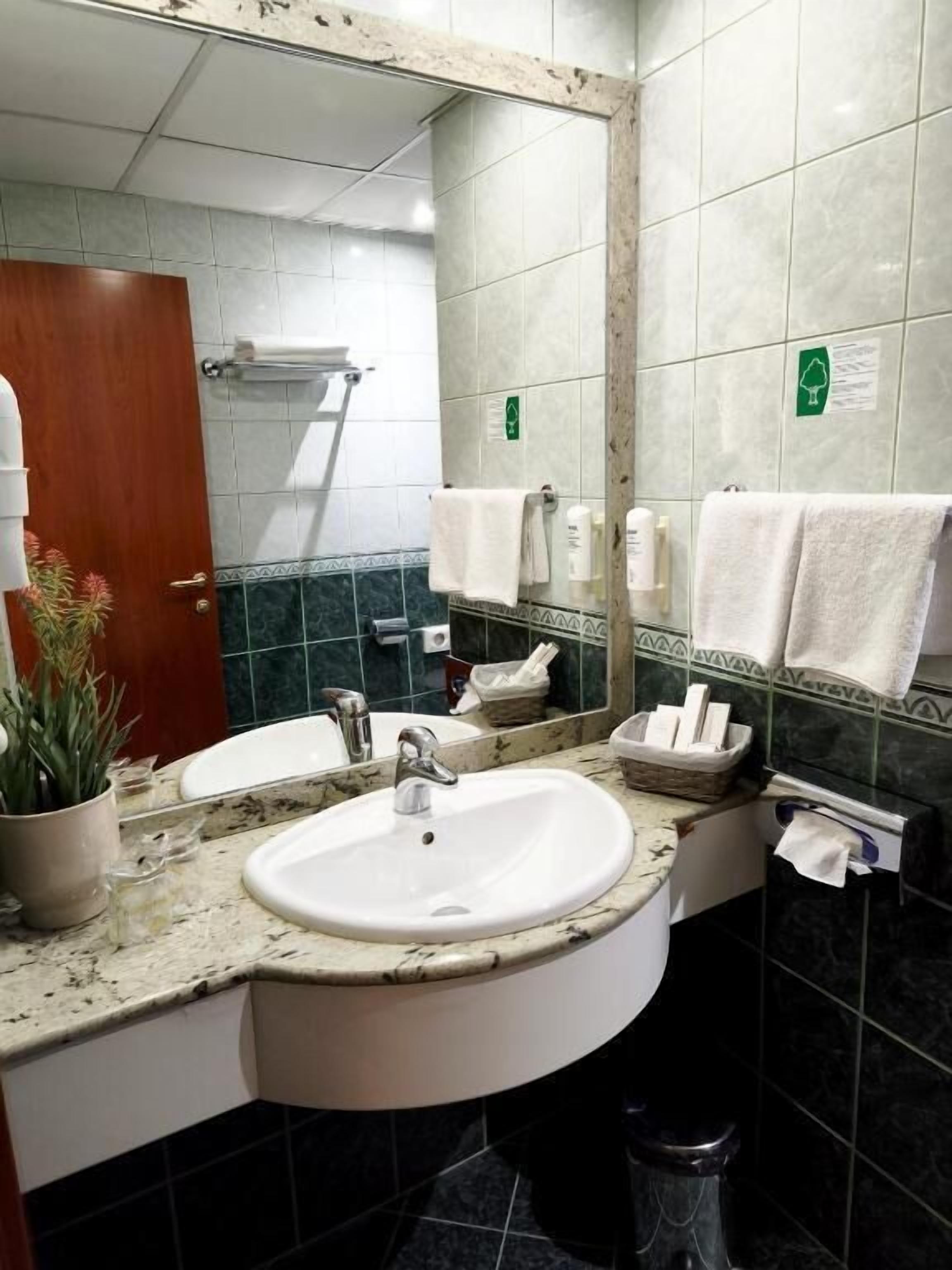 A bathroom with a sink, mirror, towel rack, and a trash bin.