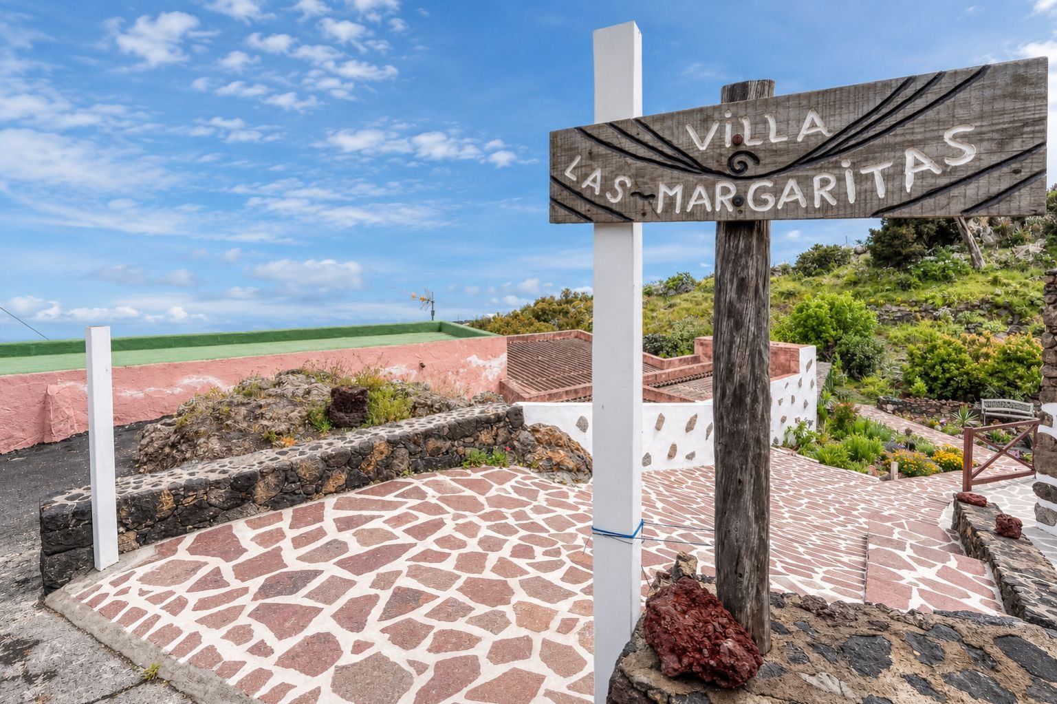 Placa de 'Villa Las Margaritas', com um pátio de pedra e vista para um campo verde.