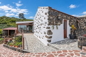 A stone house with a white exterior, a wooden door, and a stone wall.