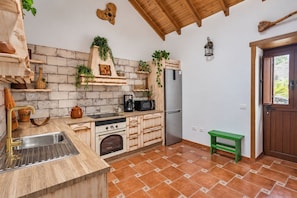 A kitchen with a brick wall, wooden cabinets, a stainless steel refrigerator, a microwave, and a green bench.