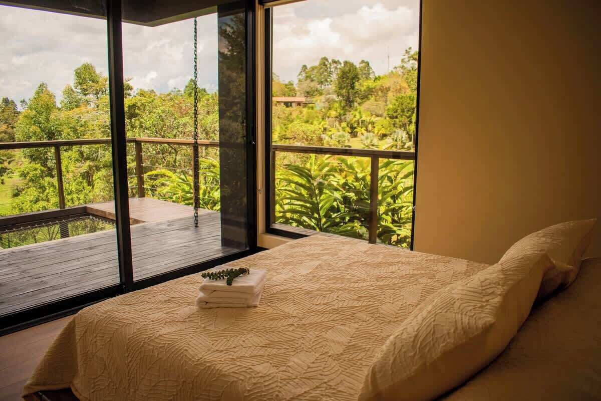 Quarto com uma janela ampla, uma cama com manta texturizada e vista para um jardim exuberante.