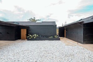 A modern building with a gravel courtyard, wooden door, and a small garden area.