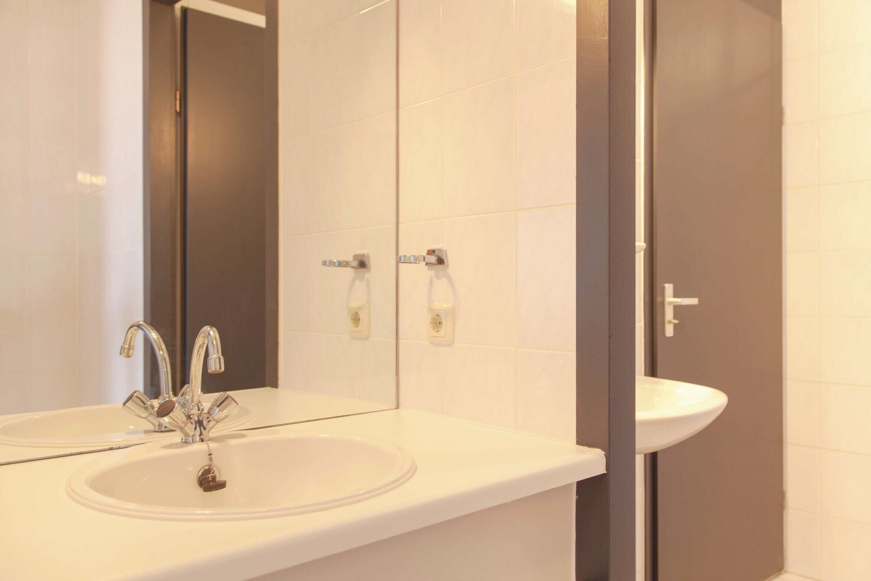Une salle de bain avec un lavabo blanc, un miroir et une porte.