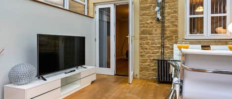 A modern living room with a flat-screen TV, a glass coffee table, and a stone wall.