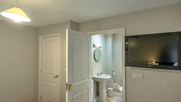 A bathroom with a toilet, sink, mirror, and a television mounted on the wall.