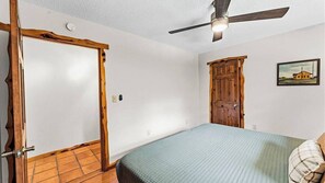 A bedroom with a bed, a ceiling fan, a wooden wardrobe, and a door.