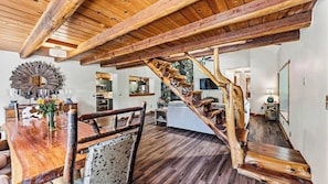 Un vaste espace de vie agrémenté d’un escalier en bois, d’une table à manger avec des chaises et d’un grand miroir.