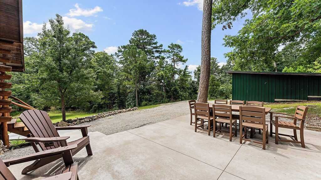 Une terrasse extérieure avec des chaises et des tables en bois, entourée d’arbres et bordée d’un chemin de gravier.