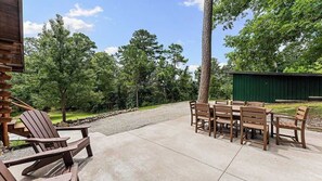 Une terrasse extérieure avec des chaises et des tables en bois, entourée d’arbres et bordée d’un chemin de gravier.