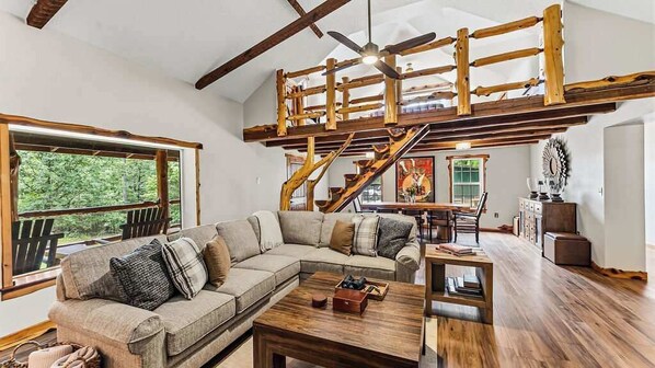 A spacious living area with a wooden staircase, a large window, and a sofa with cushions.