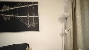 Una stanza con un letto, un comodino, una lampada, una tenda e un quadro appeso al muro.