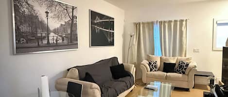 Un salon avec un canapé, une table basse, un téléviseur et un tableau accroché au mur.