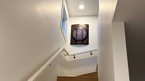 Una scala con gradini in legno e pareti bianche, che conduce a un pianerottolo con un elemento decorativo a parete.