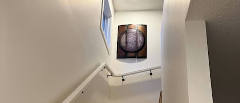 Una escalera de madera con paredes blancas que lleva a un rellano con un elemento decorativo en la pared.