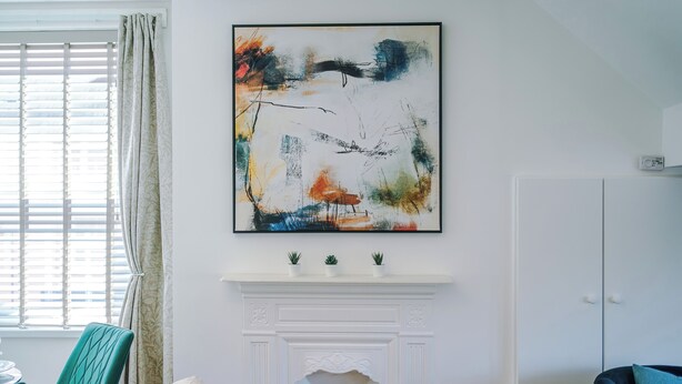 Een kamer met een open haard, een schilderij en een raam met zonwering.