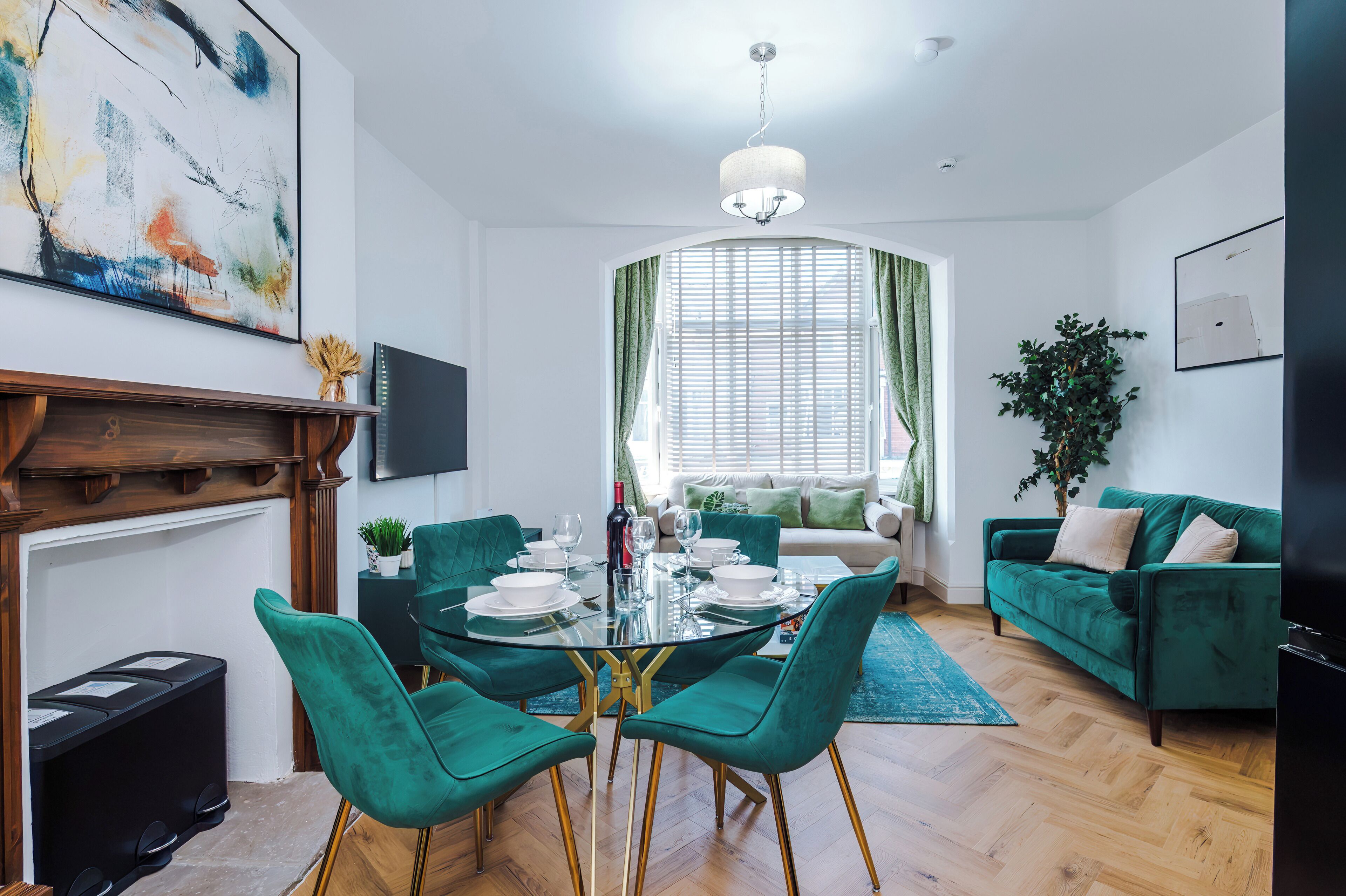 A modern living room with a dining area, green upholstered furniture, a fireplace, and artwork on the walls.