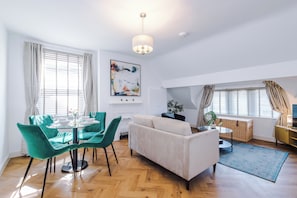 Una sala de estar con un sofá, una mesa de comedor con sillas, una chimenea y un cuadro abstracto grande en la pared.