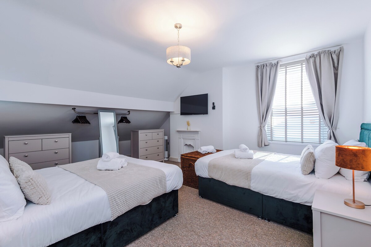 Ein Hotelzimmer mit zwei Betten, einem Flachbildfernseher, einem Spiegel, einem Schminktischchen, einem Kamin und einem Fenster mit Vorhängen.