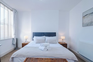 A hotel room with a large bed, two bedside tables with lamps, a radiator, and a window with blinds. - The St Annes Beach Collection (Lytham St Annes)