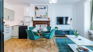 Een moderne keuken met een vaatwasser, een eethoek met een glazen tafel en blauwgroene stoelen, een flatscreen televisie en een open haard.
