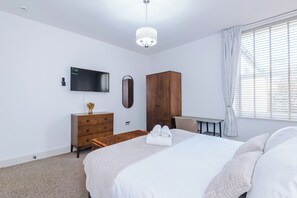 Ein modernes Schlafzimmer mit einem Bett, einem Schreibtisch, einem Kleiderschrank, einem Fernseher und einem Fenster mit Jalousien.